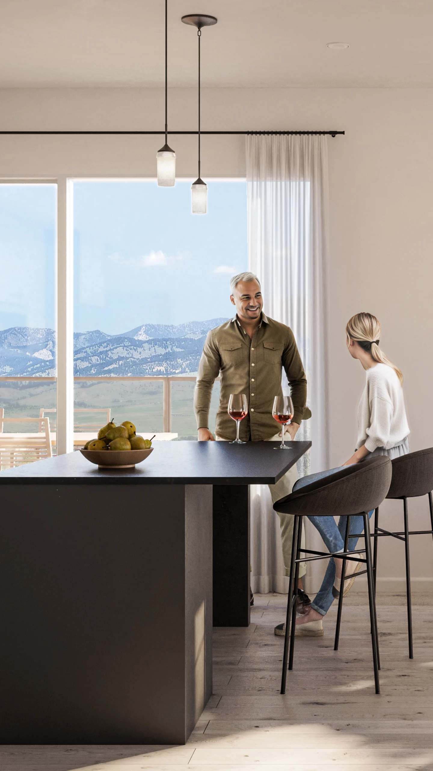 A modern open-concept living and kitchen area featuring two people enjoying drinks at a central island. The space is bright with large windows offering mountain views, and a stylish interior with neutral tones, minimalist furniture, and geometric artwork on the wall.